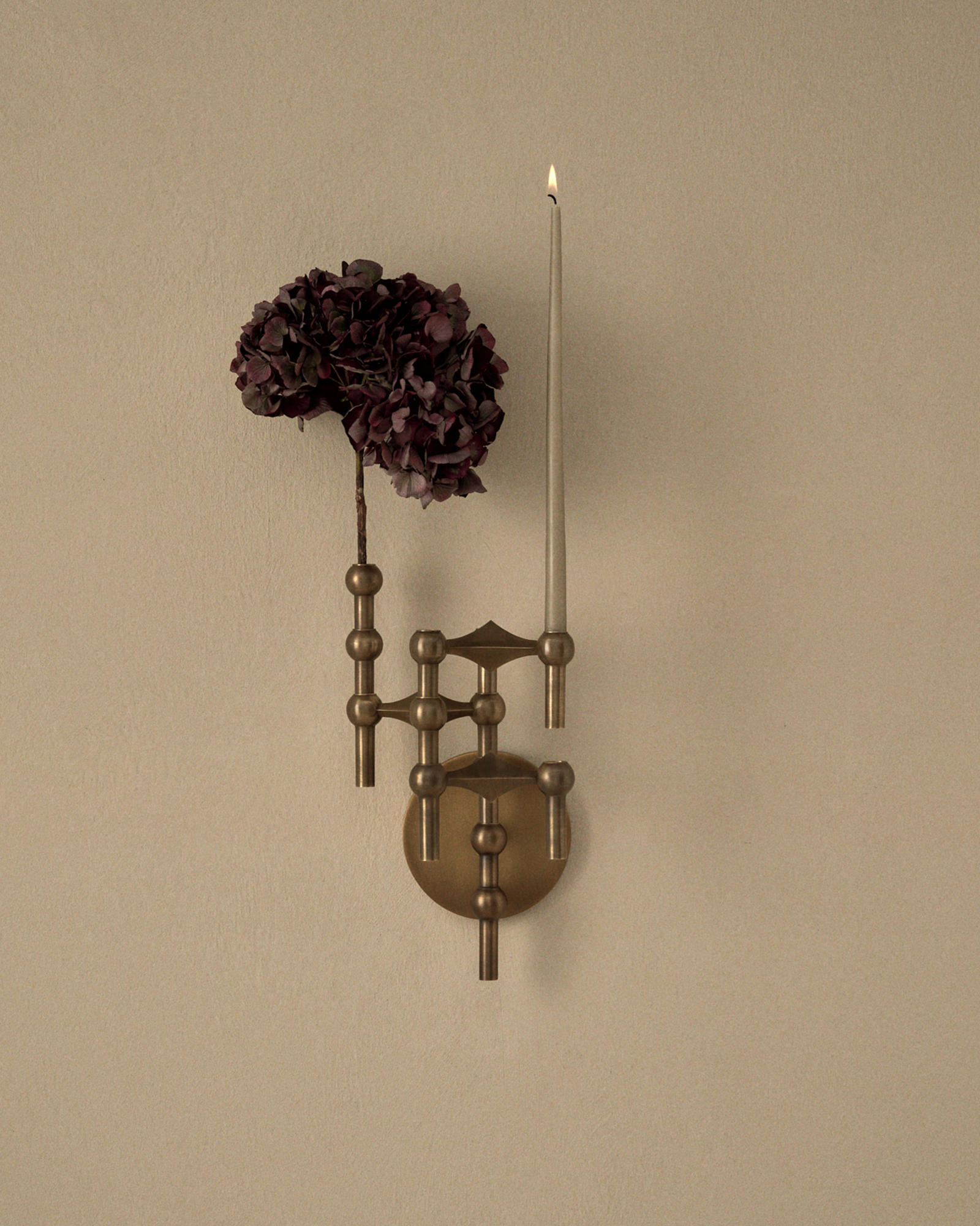 stoff nagel wall hanger in bronzed brass with nagel candle holders and vase also in bronzed brass. One lit taper candle in artichoke.