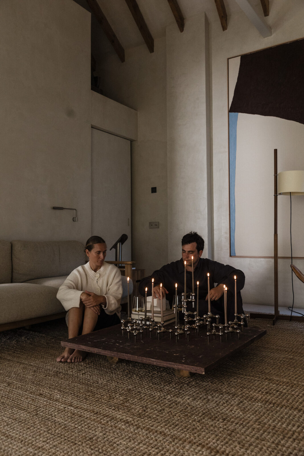 artistic duo Anton + Aiguabella in their Madrid home next to a grand candle holder sculpture of Nagel candle holders in chrome and lit taper candles.