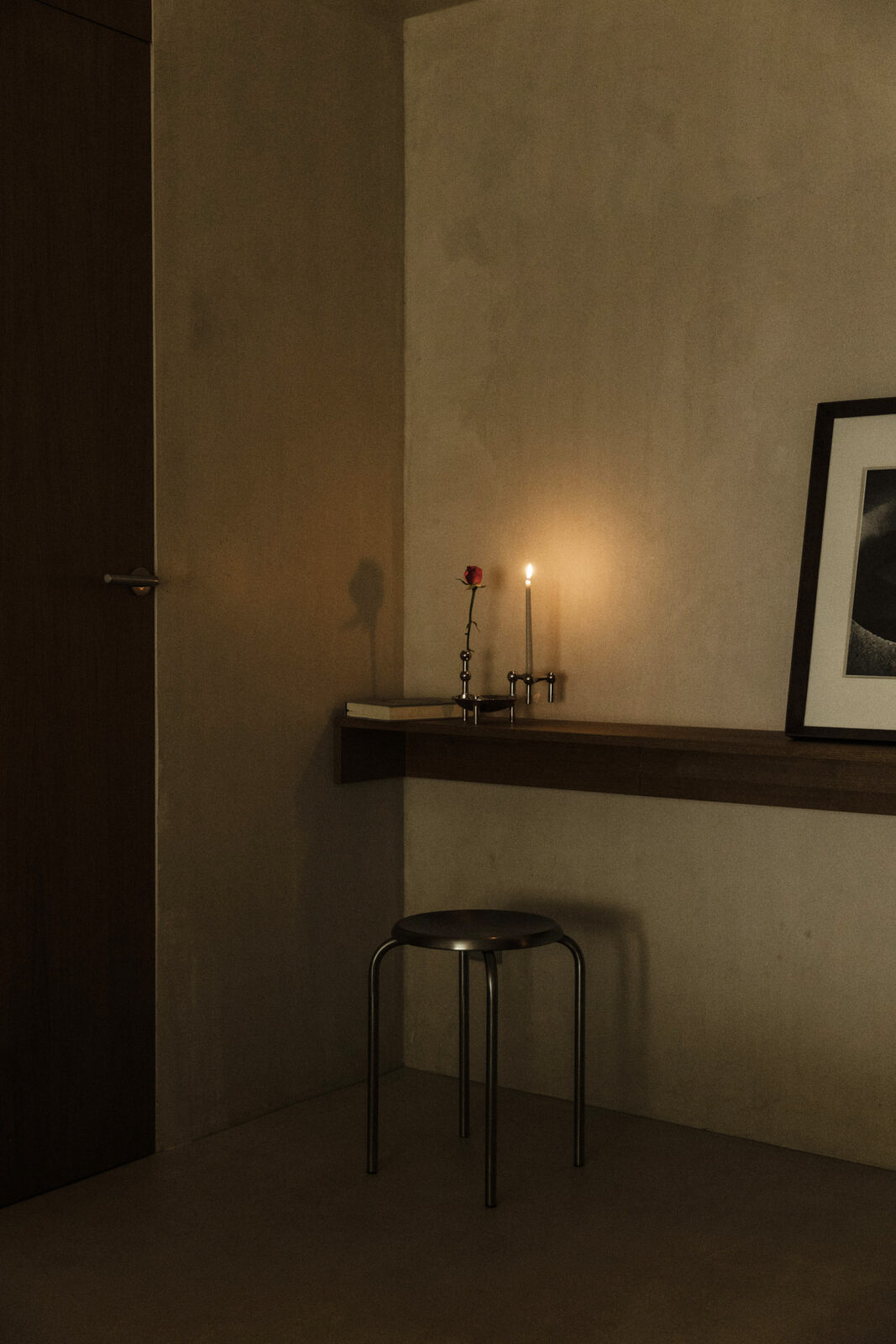 in the home of artistic duo Anton + Aiguabella with a small candle holder sculpture of Nagel candle holder in chrome, a chrome bowl and vase from STOFF Nagel and a lit taper candle.