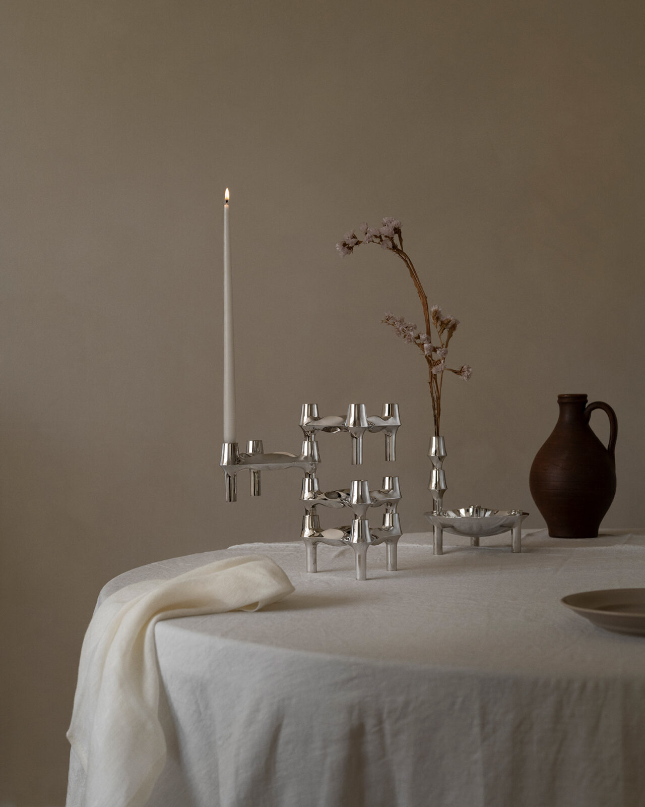 BMF candle holders in a sculptural arrangement on a dining table with the stoff nagel bowl and bmf vase in chrome. The bmf vase is styled with a flower stem.
