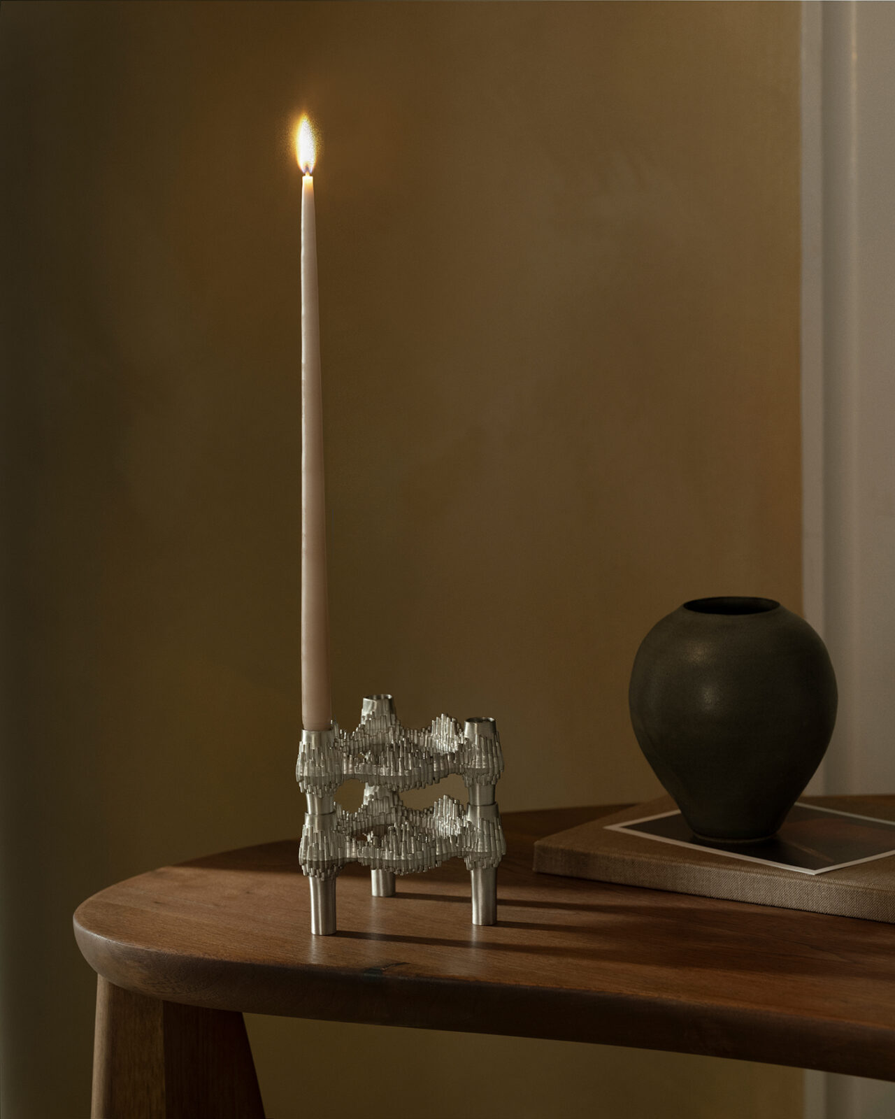 Two Quist candle holders stacked on top of each other with one lit taper candle in a table in a living room.