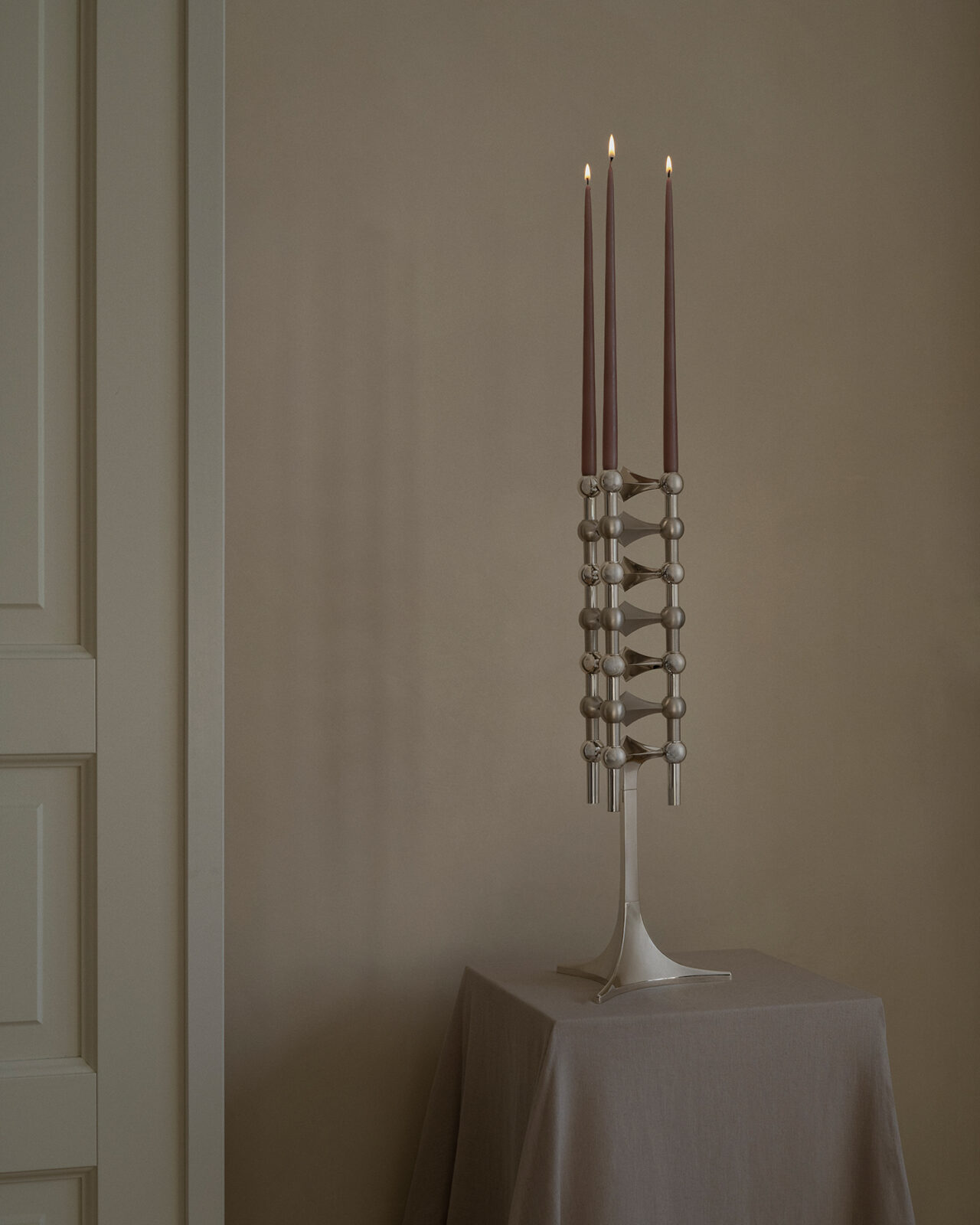 stoff nagel stand in chrome combined with nagel candle holders in chrome and brushed chrome and with three lit taper candles - a sculptural candelabra.